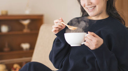 A smiling new mother enjoying a warm cup of nourishing Chinese herbal soup during her postpartum recovery in Canada 一位正在坐月的新手媽媽正喜悅地飲用溫暖滋補的中式產後調理湯水。