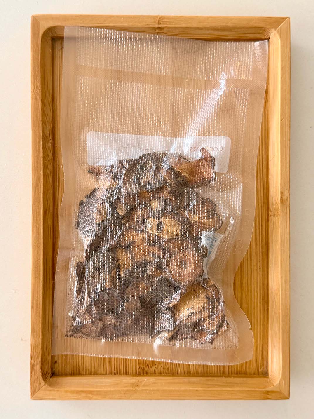 Vacuum-sealed pack of dried Chuan Xiong Szechuan lovage slices on a bamboo tray 真空密封乾製川芎根莖片，置於竹製托盤上展示
