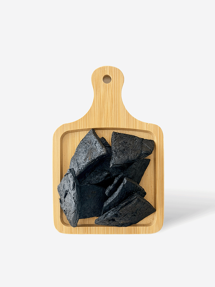 Shu Di Huang Prepared Rehmannia Root pieces displayed on a bamboo serving board 熟地炮製地黃根塊，整齊展示於竹製托盤上