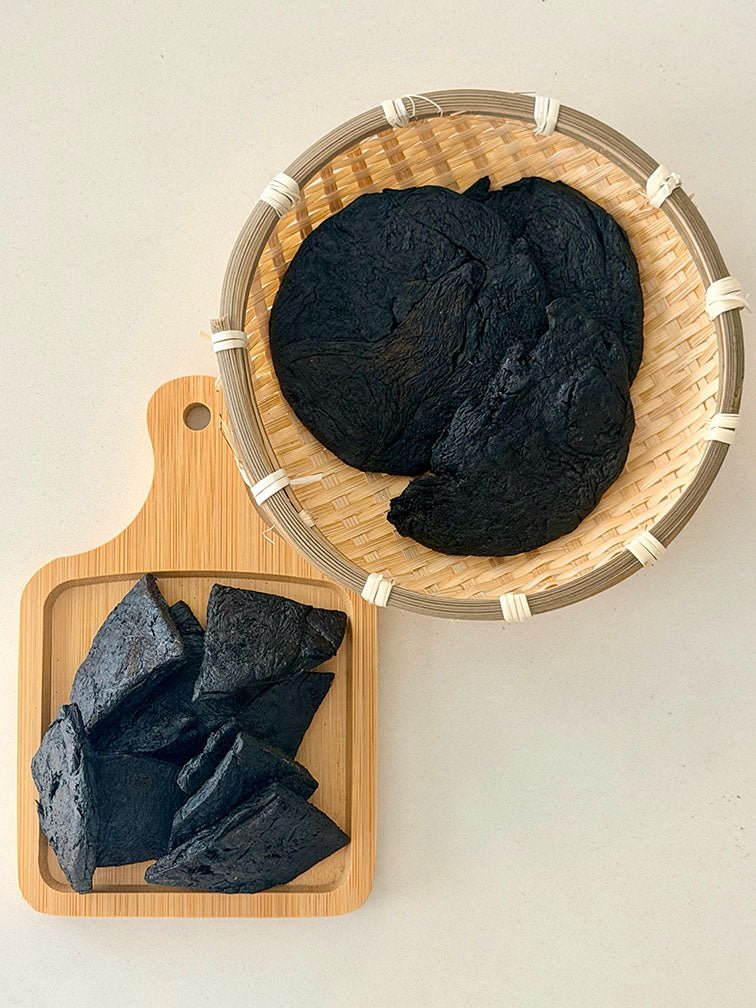 Prepared Rehmannia Root Shu Di Huang pieces displayed in a bamboo basket and wooden tray 熟地炮製地黃根塊，盛載於竹籃及木製托盤上展示