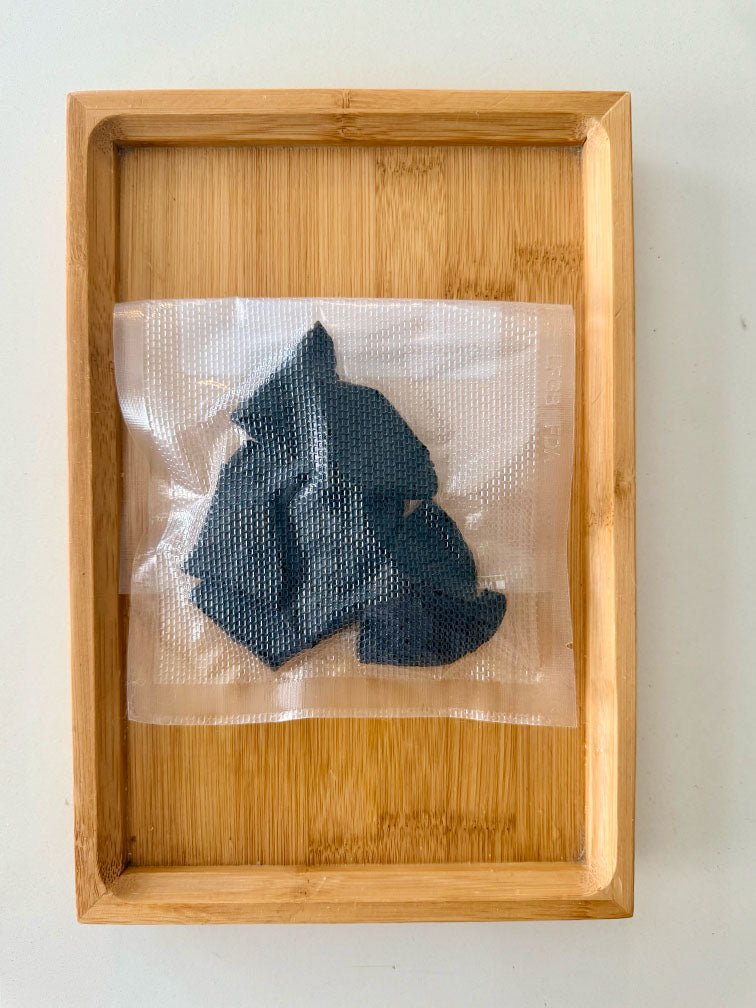 Vacuum-sealed pack of Shu Di Huang Prepared Rehmannia Root on a bamboo tray 真空密封熟地炮製地黃根，置於竹製托盤上展示