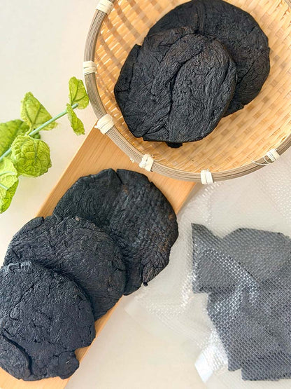 Shu Di Huang Prepared Rehmannia Root pieces in a bamboo basket beside vacuum-sealed packaging 熟地炮製地黃根塊置於竹籃中，旁邊展示真空密封包裝