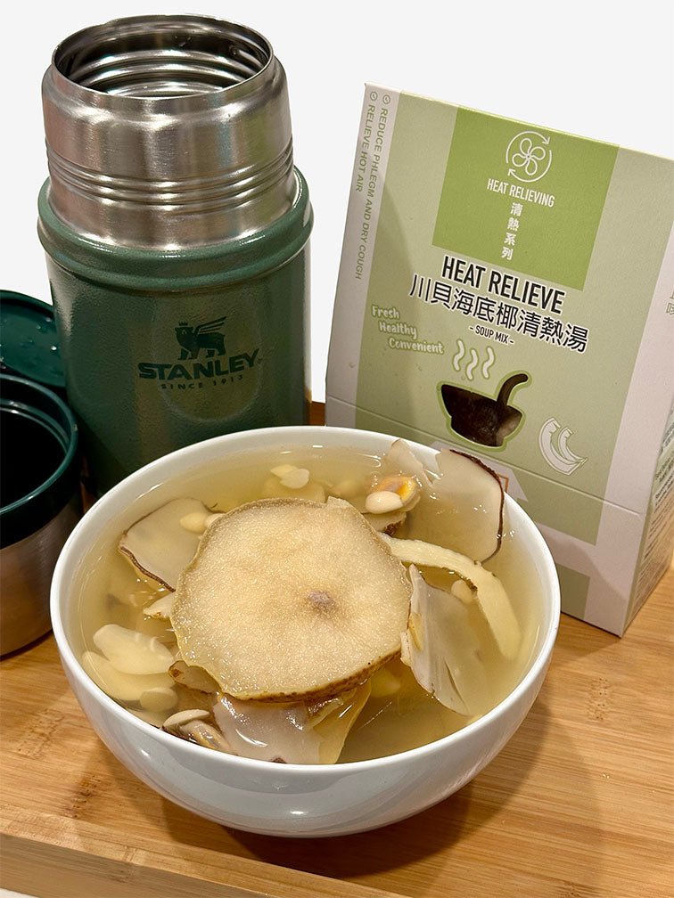 A bowl of warm soup accompanied by a Stanley food jar in Hammertone green and a heat relieve soup pack on a wooden table, creating a cozy dining atmosphere. 木桌上一碗熱騰騰的暖湯，配上Hammertone 綠色Stanley燜燒壺和清熱湯包，營造出溫馨的用餐氛圍。