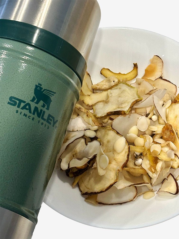 A bowl filled with heat relieve soup's ingredients and Chinese herbs placed next to a Stanley food jar in Hammertone green on a wooden surface. 一個裝滿清熱湯湯料食材的碗放在木質表面上的Hammertone 綠色Stanley 燜燒壺旁