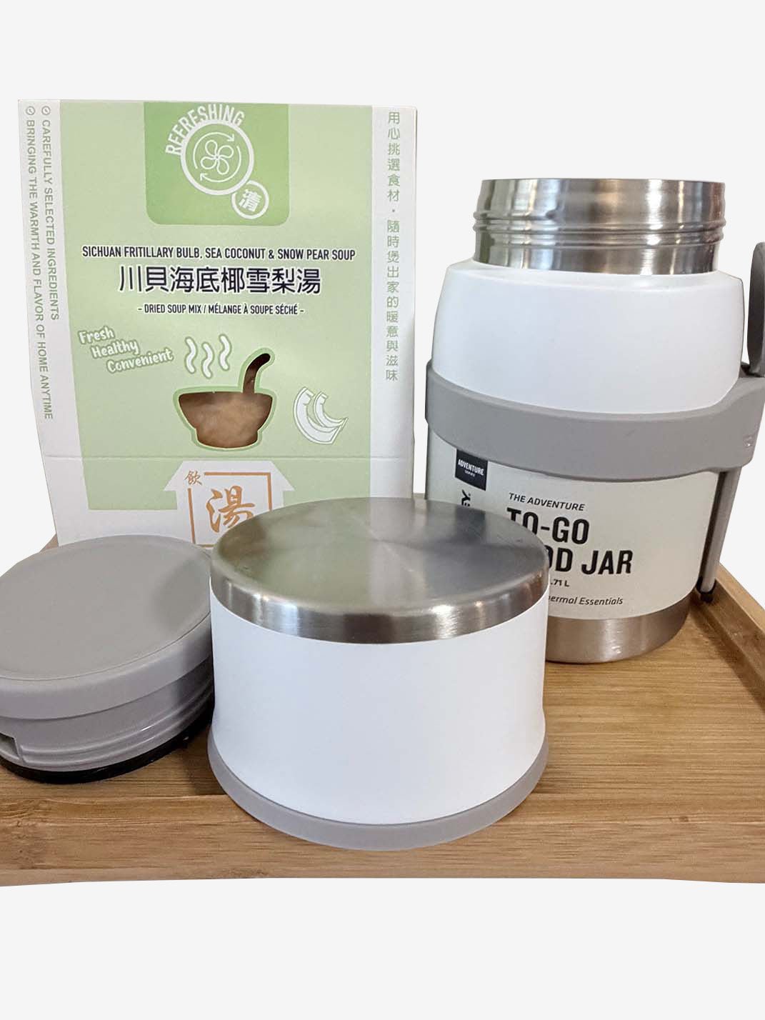 Photo on a wooden tray with a green boxed soup mix (Sichuan Fritillary Bulb, Sea Coconut & Snow Pear Soup) behind a white Stanley Adventure To-Go Food Jar; the jar is open, with a separate white container and two lids placed in front. 木托盤上的產品照：後方是一盒綠色川貝海底椰雪梨湯包，旁邊是白色 Stanley Adventure To-Go Food Jar（已開蓋），前方放有一個白色容器與兩個蓋子。